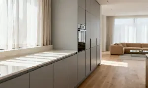 Cocina moderna con armarios grises y una encimera de mármol clara. La luz del sol entra por las cortinas, creando un ambiente acogedor.