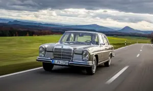 En klassisk Mercedes 60-tal glider fram på en slingrande landsväg med böljande gröna fält och dramatiska berg i bakgrunden.