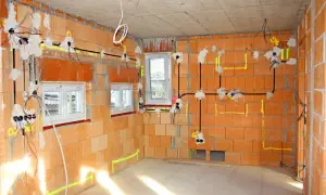 Rozpoczyna się instalacja elektryczna w nowym budynku. Widać przewody, puszki i oznaczenia na ceglanych ścianach.