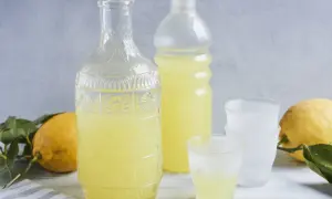 Ein Glas mit dem original italienischen Limoncello Rezept, daneben eine Karaffe, Flasche und Zitronen.
