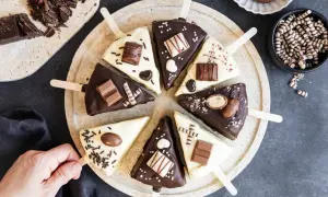Schokoladige Cheesecake-Sticks, verziert mit Schokoriegeln und Streuseln, auf einem Teller arrangiert.