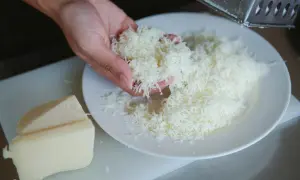 Ręka trzyma starty ser koryciński, przygotowywany według tradycyjnego przepisu.