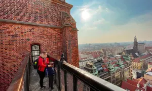 Kobieta z dzieckiem na moście pokutnic we Wrocławiu podziwia panoramę miasta.