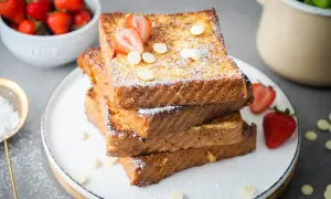 Gestapelte French Toast Scheiben, bestäubt mit Puderzucker und garniert mit Erdbeeren und weißen Schokoladenchips.