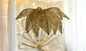 Złota lampa z koralików diy w kształcie liścia, wisząca na tle białych zasłon i migoczących światełek.