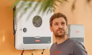 Hombre mirando hacia arriba junto a un inversor Fronius GEN24, símbolo de energía solar eficiente y sostenible.