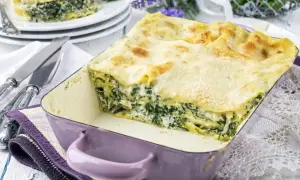 Pyszne lasagne ze szpinakiem w fioletowym naczyniu, gotowe do podania. Obok sztućce i dekoracyjne kwiaty.