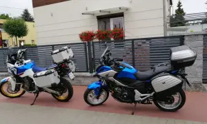Dwa motocykle turystyczne z kuframi stoją przed nowoczesnym domem z kwiatami na balkonie.