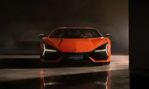 Pomarańczowy Lamborghini Revuelto z ostrymi światłami Y, stojący na błyszczącej podłodze w ciemnym pomieszczeniu.
