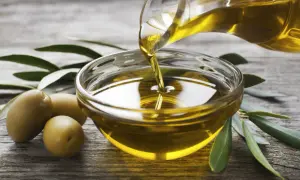 Olio evo l'extravergine, dorato e puro, viene versato in una ciotola di vetro. Olive e foglie di ulivo completano la scena.