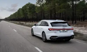 Białe Audi A5 Avant 2025 pędzi pustą drogą wśród sosnowego lasu.