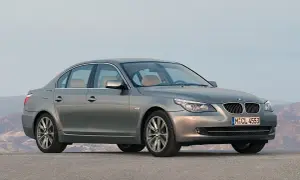 Szary sedan BMW 5 Series (E60) z jasnym wnętrzem stoi na pustej drodze, z górami w tle.