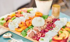 Eine üppige italienische Brotzeit mit Burrata, Tomaten, Pfirsichen, Kirschen und Prosciutto auf einem Holzbrett.