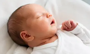 Słodki noworodek je krótko i zasypia, wtulony w białe pieluszki. Jego małe rączki są zaciśnięte w piąstki.