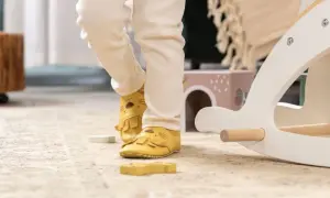 Nóżki dziecka w żółtych kapciach z motywem lwa na dywanie obok drewnianej konika na biegunach.