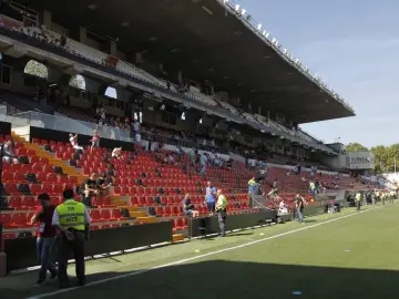 Puste trybuny stadionu Vallecas, z kilkoma osobami siedzącymi i stojącymi.