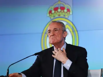 Florentino Pérez, prezes Realu Madryt, w garniturze, z ręką na szyi, na tle logo klubu.