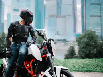 Motocyklista w zbroi ochronnej siedzi na motocyklu na tle wieżowców.