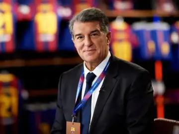 Uśmiechnięty prezes Barcelony, Joan Laporta, w garniturze, z identyfikatorem FC Barcelona na szyi.