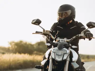 Motocyklista w kasku i kurtce siedzi na motocyklu na tle krajobrazu.