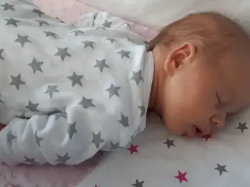 Słodki noworodek śpi z otwartą buzią, ubrany w pajacyk w gwiazdki.