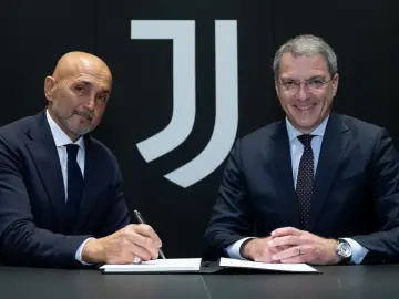 Dwóch mężczyzn w garniturach siedzi przy stole. Jeden z nich, łysy, podpisuje dokument. Za nimi logo Juventusu.