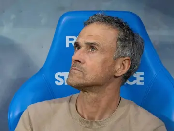 Luis Enrique, kto jest trenerem PSG, siedzi na niebieskiej ławce, zamyślony.