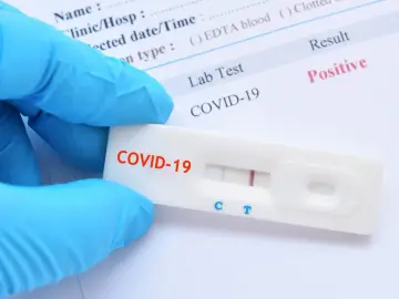 Ręka w niebieskiej rękawiczce trzyma test antygenowy COVID-19 z dwoma widocznymi liniami, co oznacza pozytywny wynik.