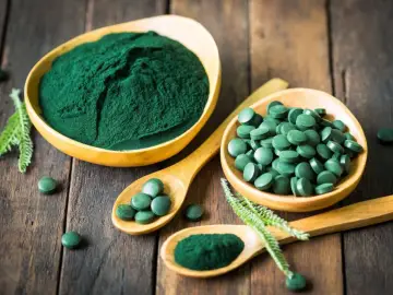Chlorella vs spirulina: zielony proszek i tabletki na drewnianym tle. Dwa rodzaje alg w formie suplementów diety.
