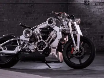 Wyjątkowy, lśniący motocykl, prawdopodobnie najdroższy motor na świecie, z masywnym silnikiem i detalami z polerowanego metalu, na tle ceglanej ściany.