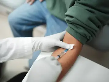 Pobieranie krwi do badań, które mogą pomóc w diagnostyce trzustki. Lekarz w rękawiczkach pobiera krew strzykawką.