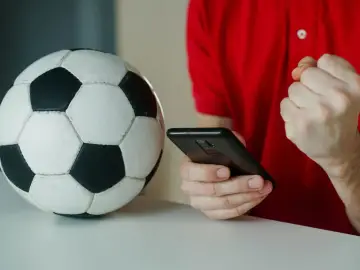 Piłka nożna i smartfon. Kibic sprawdza wynik, licząc na powyżej 2.5 gola.