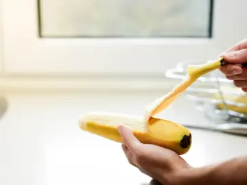 Dłoń obiera banana. Pamiętaj, z czym nie łączyć potasu, by uniknąć problemów zdrowotnych.