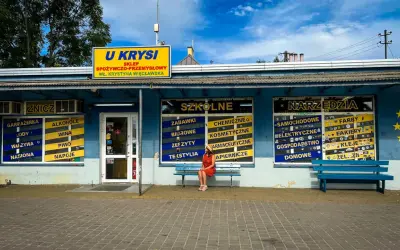 Dziewczyna w czerwonej sukience siedzi na ławce przed sklepem "U Krysia", gdzie kręcono "Ranczo".