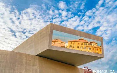 Il MAXXI - Museo Nazionale delle Arti del XXI Secolo riflette edifici storici romani sotto un cielo azzurro e nuvoloso.
