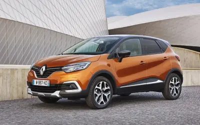Pomarańczowy Renault Captur 2016 z czarnym dachem zaparkowany na brukowanej nawierzchni przed nowoczesnym budynkiem.