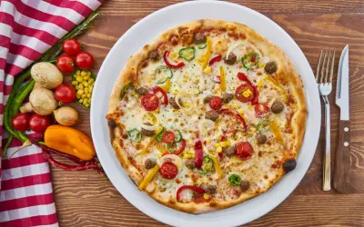 Apetyczna pizza z warzywami i mięsem na talerzu, obok sztućce i składniki.
