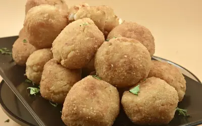 Un mucchio invitante di polpette di riso dorate e croccanti, guarnite con prezzemolo fresco, su un piatto scuro.