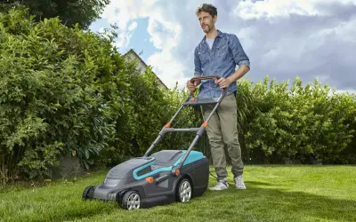 Mężczyzna z kosiarką elektryczną, która jest jedną z najlepszych kosiarek elektrycznych, dba o swój zielony trawnik.