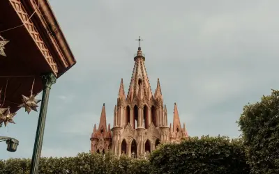 Imponująca iglica kościoła w San Miguel, otoczona zielenią, z ozdobnymi gwiazdami zwisającymi z zadaszenia.