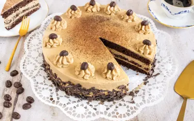 Eine köstliche Mokka Torte, verziert mit Kaffeebohnen und Schokostückchen, wartet auf Genießer. Daneben ein Stück Torte und eine Tasse Kaffee.