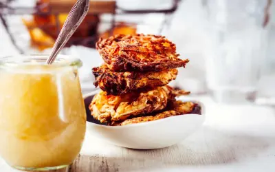 Goldbraune Kartoffelpuffer stapeln sich in einer Schüssel, daneben ein Glas Apfelmus. Ein perfektes Kartoffelpuffer Rezept für jeden Anlass.