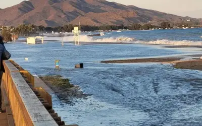 El espigón Garrucha bajo el agua, con olas rompiendo y montañas al fondo.