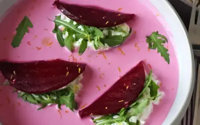 Vacker vegetarisk mat: rödbetor, ruccola och färskost i en rosa soppa, garnerad med rivet citronskal.