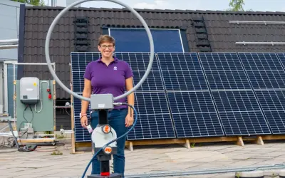 Kvinna med glasögon står framför solpaneler. Ett solceller montagesystem är synligt på taket.