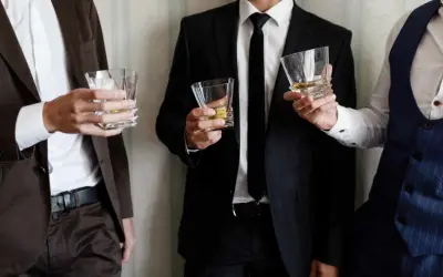 Uomini eleganti con bicchieri di whisky, perfetti per un dress code cocktail.