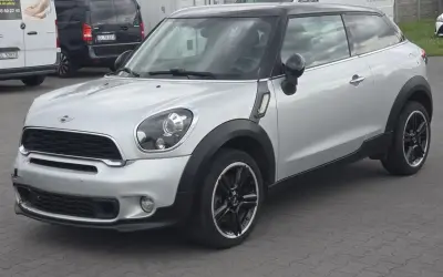 Srebrny mini paceman z czarnym dachem i felgami, zaparkowany na placu.