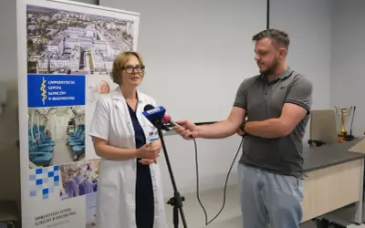 Lekarka w kitlu udziela wywiadu dziennikarzowi przed banerem Uniwersyteckiego Szpitala Klinicznego w Białymstoku.