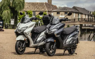 Dwa skutery Suzuki Burgman 125, jeden biały, drugi grafitowy, stoją obok siebie. Sprawdź suzuki burgman 125 cena!