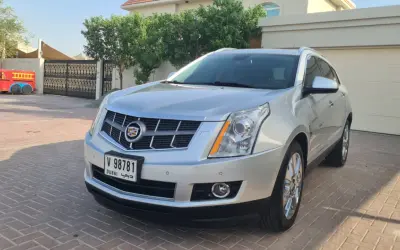 Srebrny Cadillac SRX z Dubai stoi na podjeździe przed domem. Obok widać bramę i fragment czerwonej zabawki.